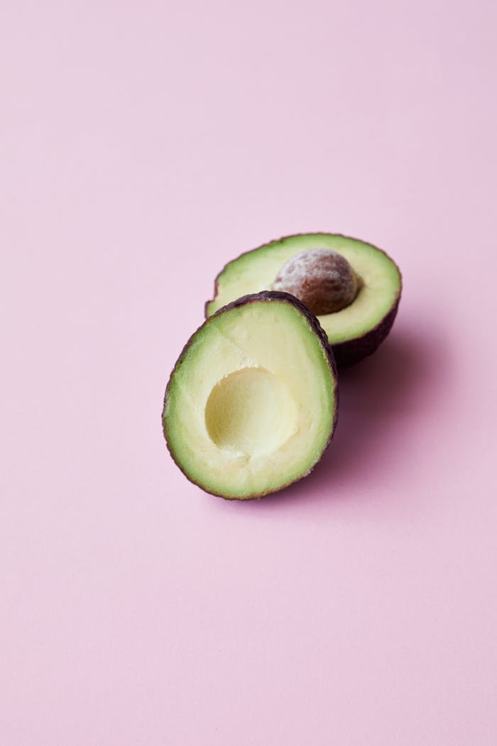 A fresh halved avocado displayed on a pastel pink surface, perfect for healthy food concepts.